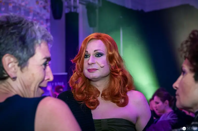 Drag Performer in Vibrant Nightclub Lighting Amid Engaged Conversation