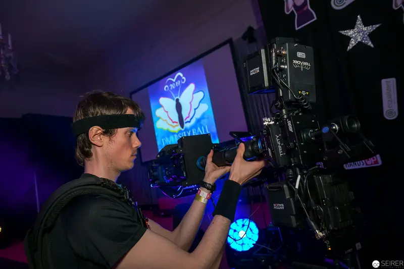 Videographer Operating Professional Camera Under Blue Stage Lighting