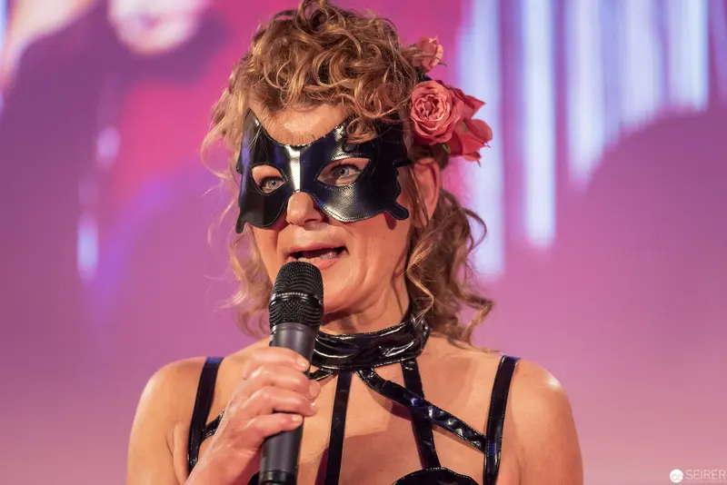 Performer in Masquerade Mask and Floral Headpiece Singing on Stage