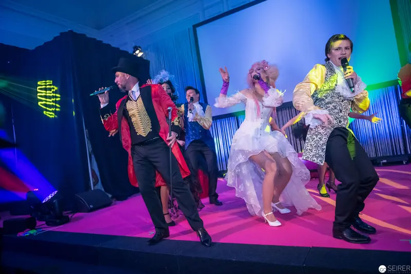 Theatrical Performance with Performers in Vibrant Costumes on Pink Stage