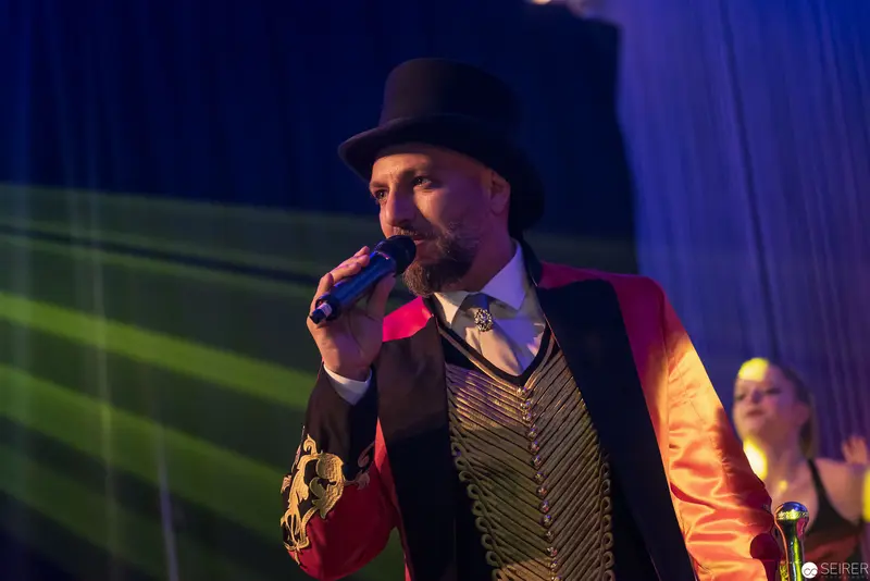 Performer in Theatrical Ringmaster Attire Singing with Microphone on Colored Stage