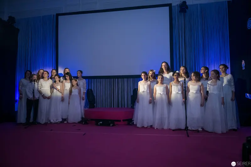 White-Robed Choir Ensemble Positioned Dramatically on Blue-Lit Stage with Projection Screen
