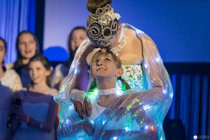 Illuminated Performers in Theatrical Embrace with Decorative Mask and Lights