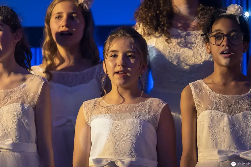 Young Choir Performers in White Lace Dresses Under Blue Stage Lighting