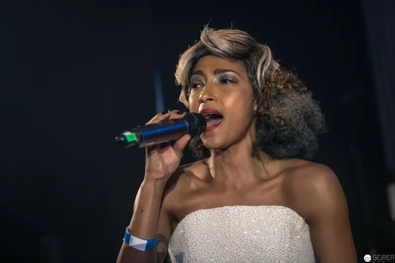 Performer in Strapless White Dress Singing Passionately into Microphone on Dark Stage