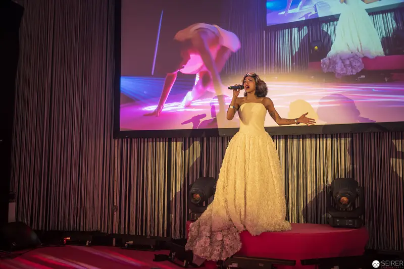 Performer in Yellow Gown Singing on Stage with Dramatic Multimedia Backdrop