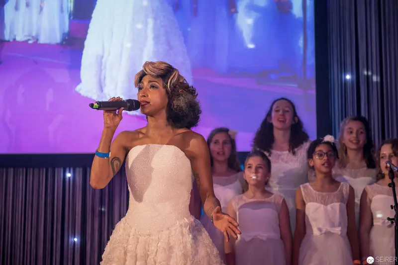 Young Female Vocalist in White Performing with Children's Choir on Stage