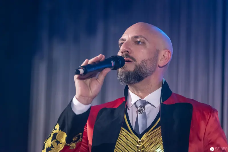 Performer in Red Jacket Singing Passionately with Microphone on Stage