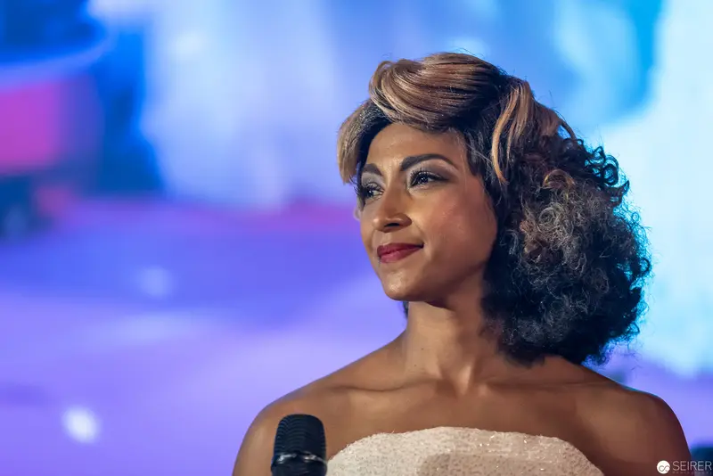 Performer in White Strapless Gown Holding Microphone Against Blue Backdrop
