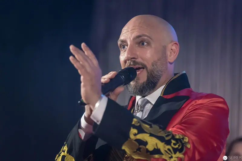 Theatrical Performer in Red Jacket Gesturing Dramatically During Stage Performance