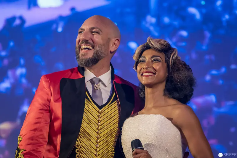 Jubilant Performers on Stage with Vibrant Backdrop and Dramatic Costumes