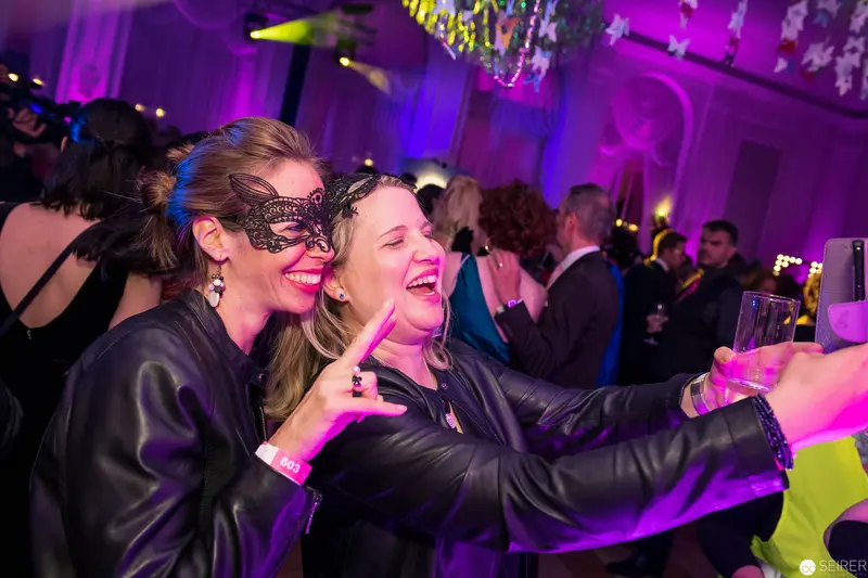 Masked Woman and Friend Laughing at Vibrant Masquerade Party
