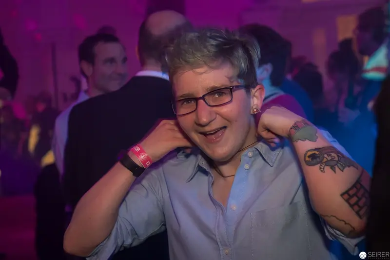 Jubilant Partygoer in Purple-Hued Nightclub Scene with Tattoos and Glasses