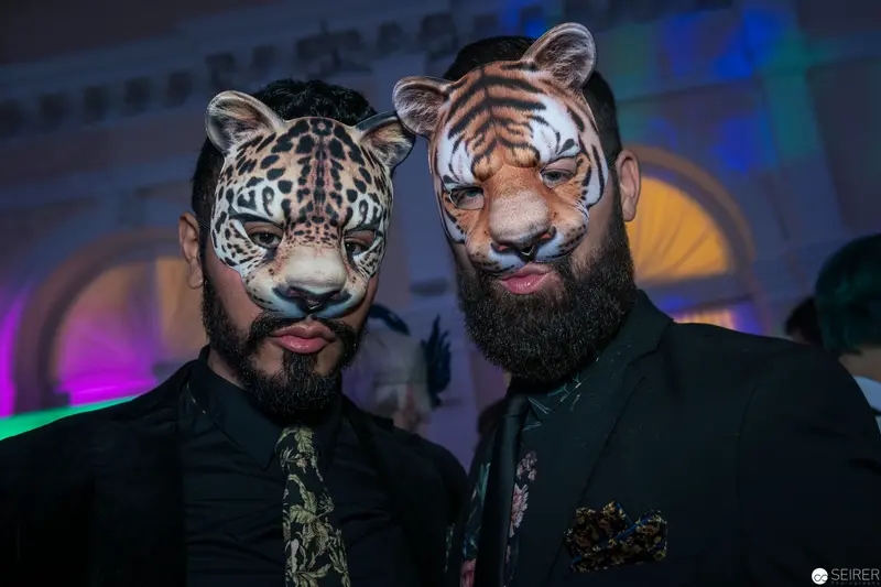 Two Men in Feline Masks at Costumed Event, Dramatic Lighting and Colorful Backdrop