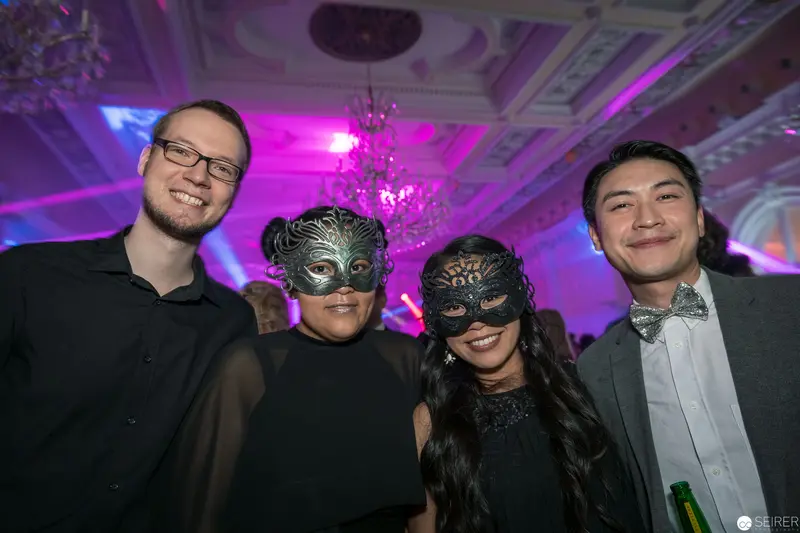 Masked Revelers in Lavender-Lit Ballroom During Formal Masquerade Event