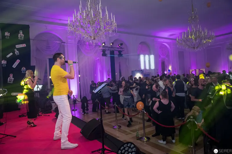 Yellow-Shirted Performer on Purple-Lit Stage with Elegant Chandeliers