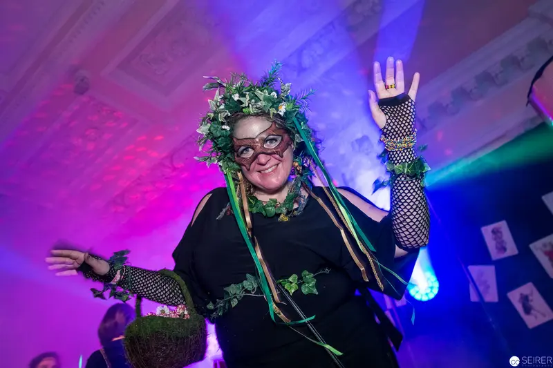 Festive Performer in Botanical Headdress and Fishnet Styling Under Colorful Stage Lights