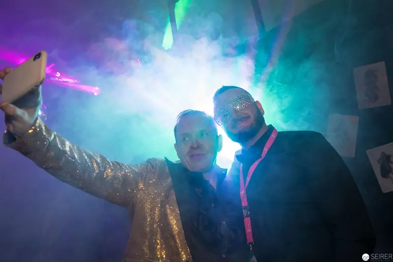 Glittering Duo Posing During Nighttime Event with Colorful Atmospheric Lighting