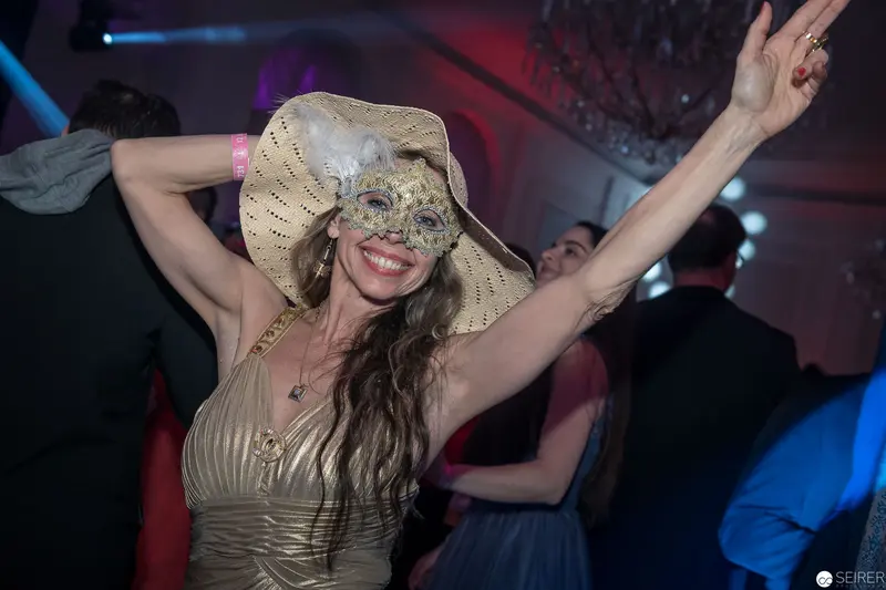 Masked Woman Dancing at Festive Evening Event in Glamorous Gold Dress