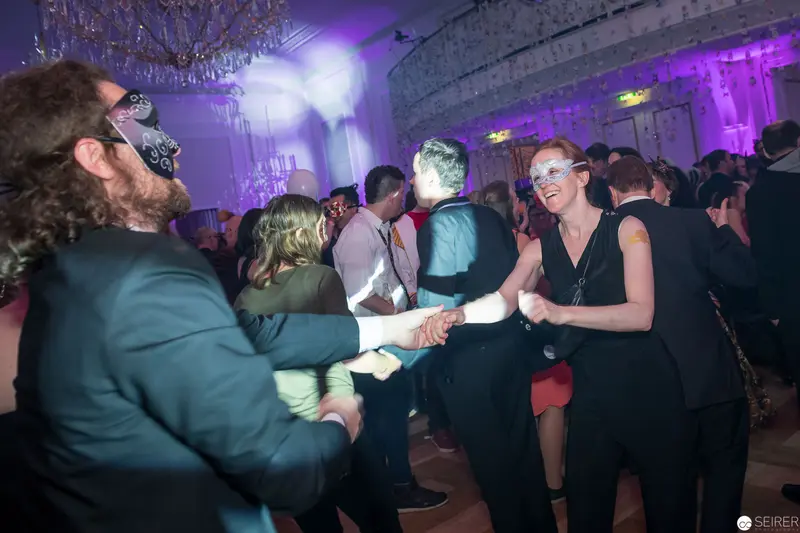 Masked Revelers Dancing at Formal Evening Event with Purple Lighting