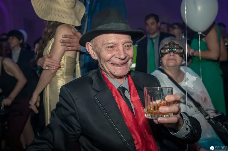 Elderly Gentleman in Fedora Enjoying Festive Party with Cocktail and Vibrant Atmosphere