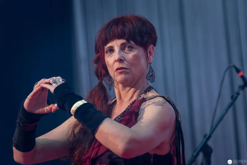 Performer in Red with Expressive Gesture on Dimly Lit Stage