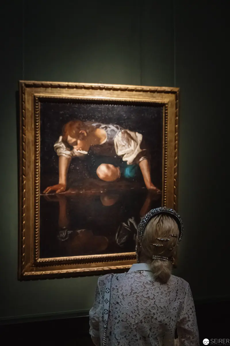 Viewer Contemplates Caravaggio's Narcissus at Kunsthistorisches Museum Wien Exhibition