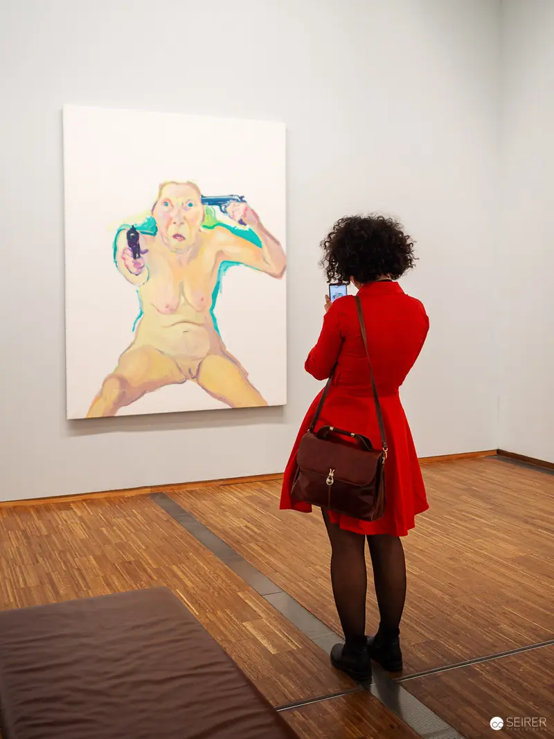 Maria Lassnig Exhibition: Viewer in Red Coat Contemplating Figurative Artwork at Albertina