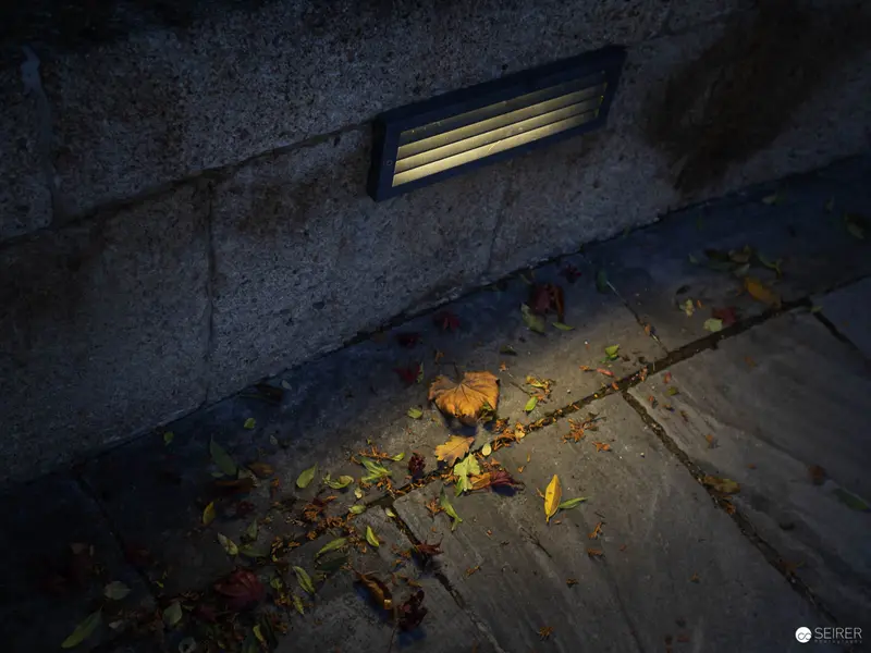 Autumn Nocturne: Illuminated Ventilation Grate amid Fallen Leaves