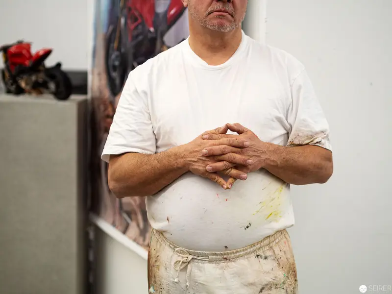Worker in White T-Shirt with Paint-Stained Apron Clasping Hands Over Abdomen