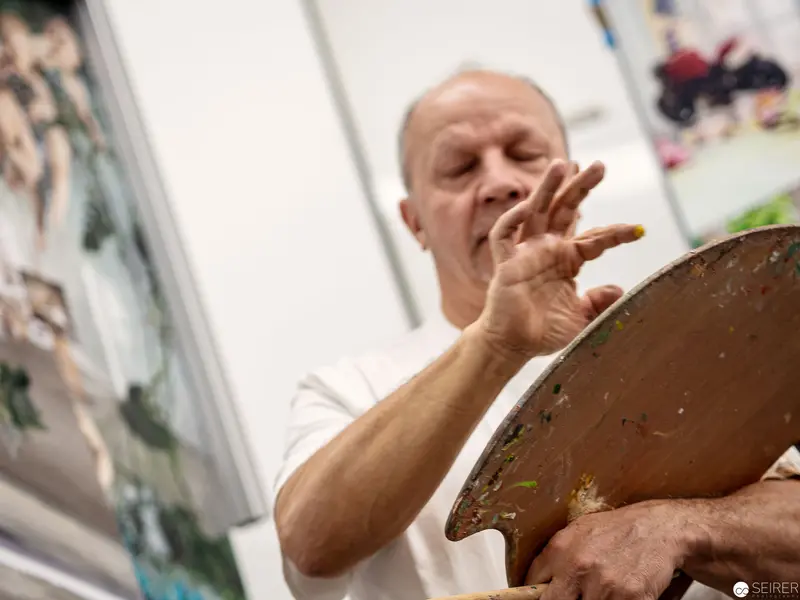 Artist in White Gesturing While Holding Paint Palette in Studio Setting