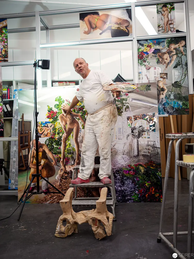 Artist in White Standing on Carved Wooden Support amid Eclectic Studio Environment