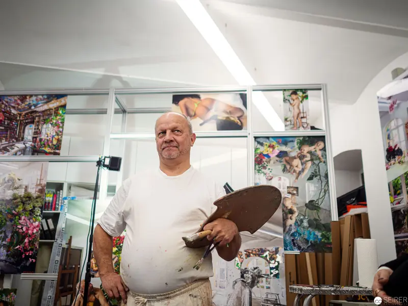 Artist in White Studio, Holding Painting Tool Amid Colorful Artworks
