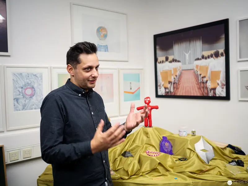 Designer Demonstrates Interactive Sculpture on Yellow-Draped Surface with Gallery Artworks