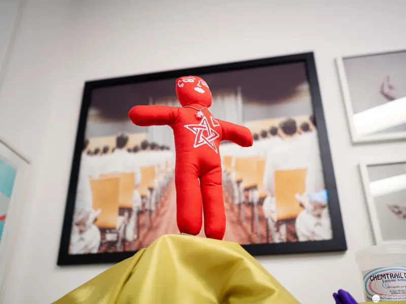 Red Voodoo Doll Positioned Against Framed Photographic Backdrop