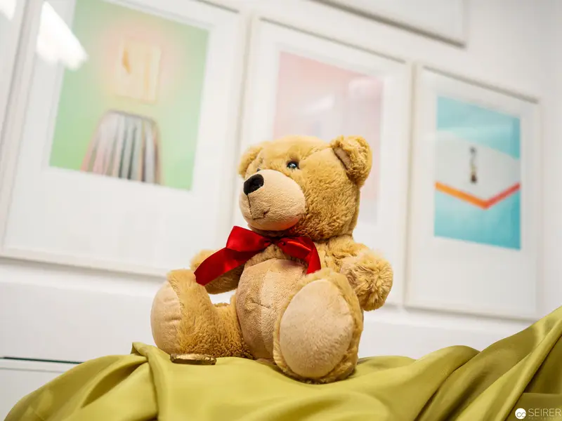 Teddy Bear with Red Bow Seated on Yellow Fabric Against Pastel Artwork