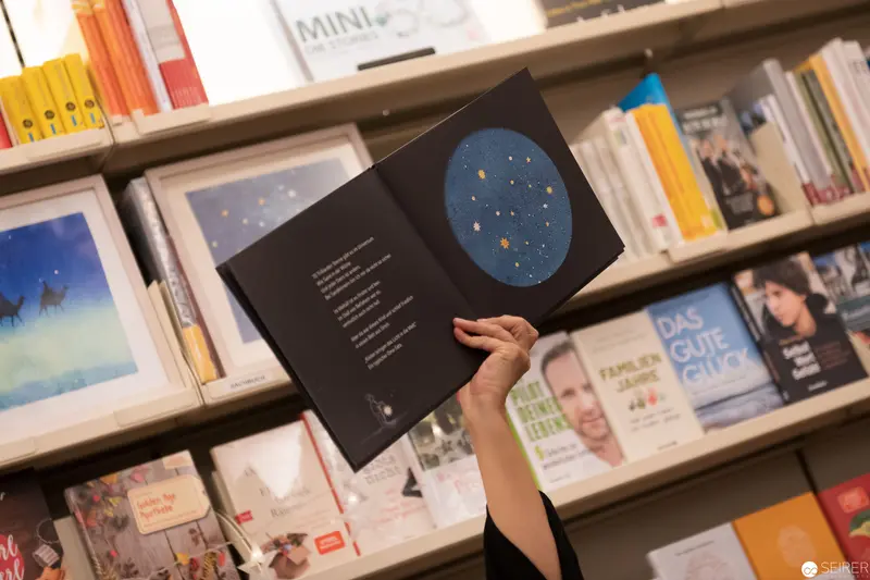 Visitor Holding Open Book with Star Map in Bookstore
