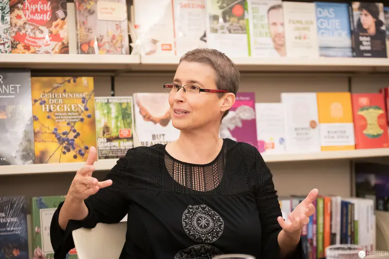Woman Speaking at Bookstore Event with Library Shelves Behind