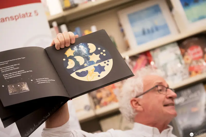 Man Displaying Moon Phase Illustration in Library or Gallery Setting