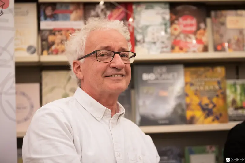 Man with White Hair and Glasses Smiling in Front of Shelved Display