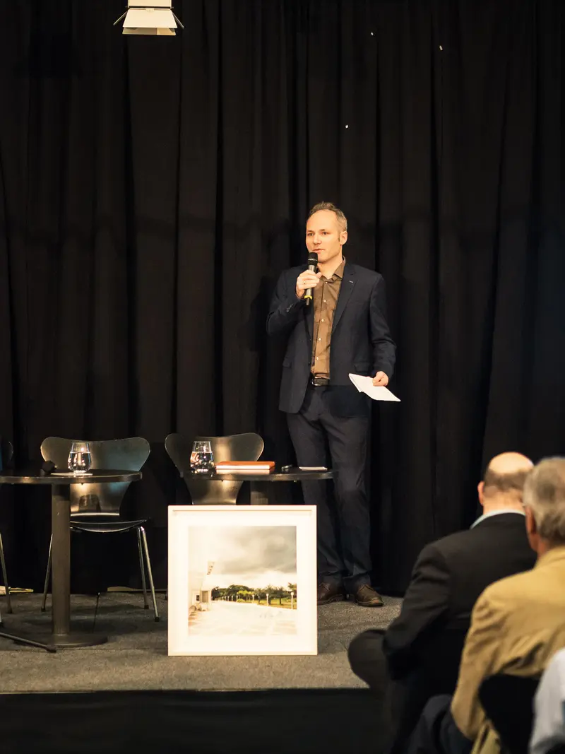 Public Speaker Presenting at Conference with Framed Artwork and Attentive Audience