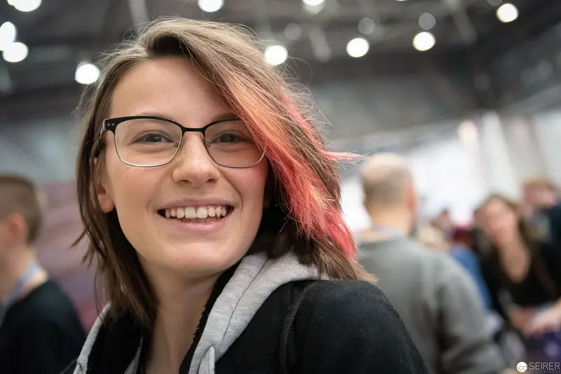 Young Attendee Smiling at Vienna ComicCon 2019, Glasses and Pink-Highlighted Hair