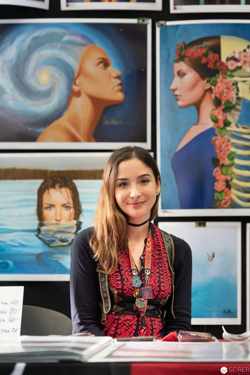 Young Artist Seated Amid Surrealist Portrait Gallery Displaying Vibrant Artwork