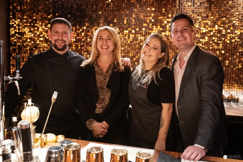 Four Hospitality Professionals Posing at Elegant Metallic-Backdrop Bar
