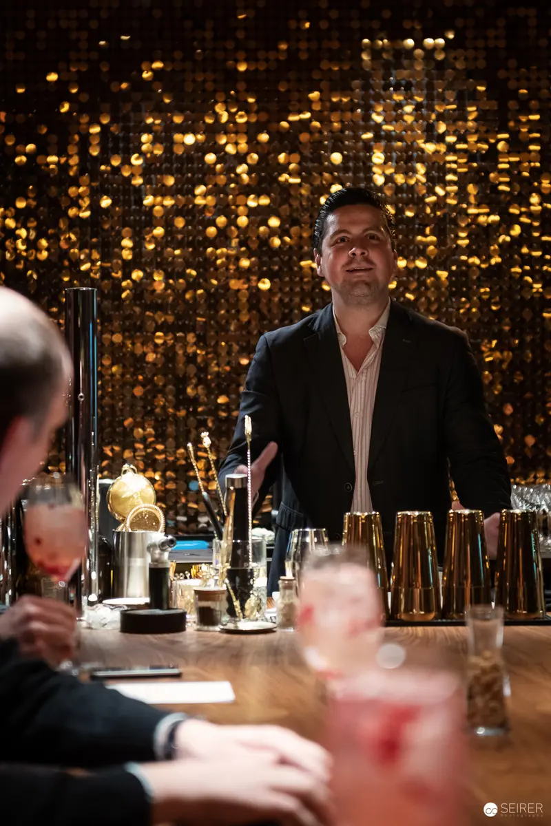 Bartender Illuminated by Golden Sequined Backdrop at Exclusive Cocktail Venue