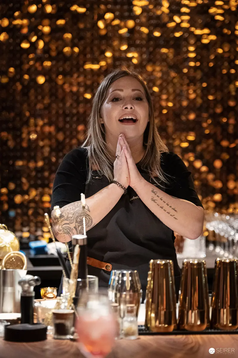 Bartender in Black Gesturing Dramatically Behind Illuminated Golden Bar