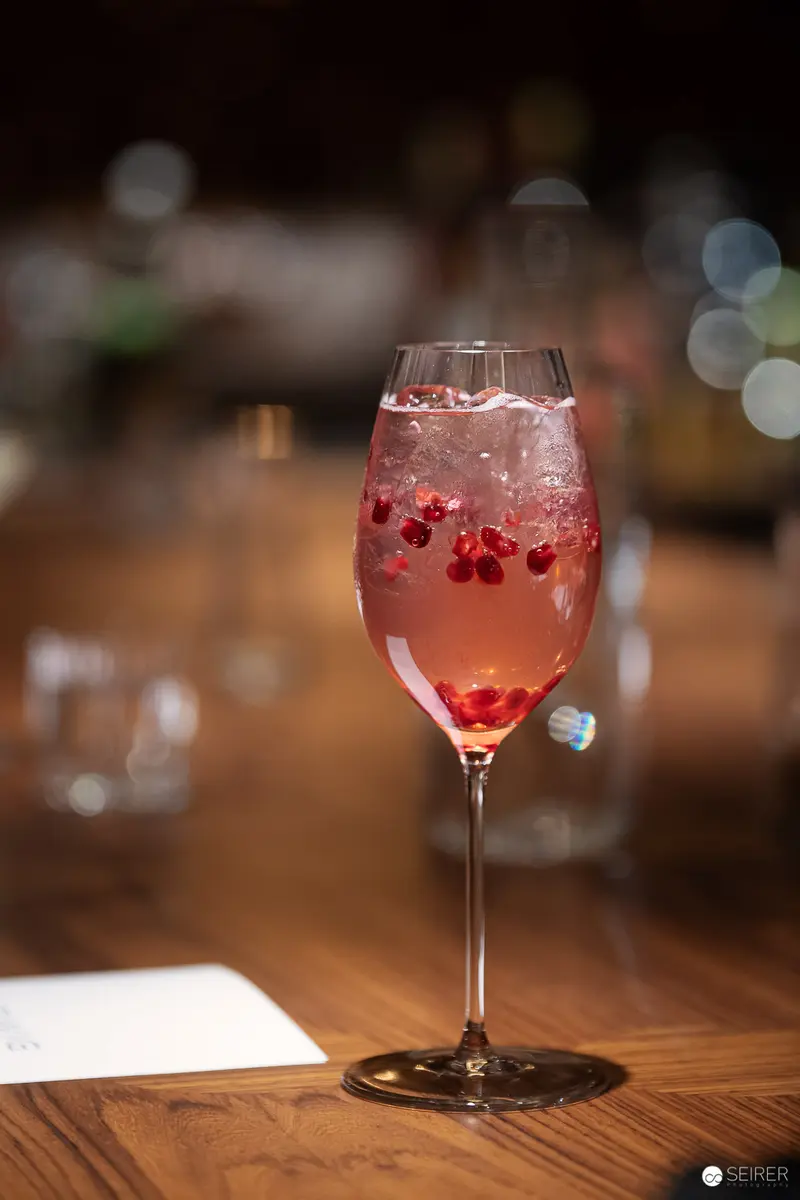Ruby-Studded Cocktail in Crystalline Stemware on Rustic Wooden Surface