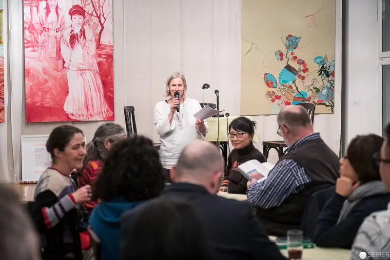 Literary Reading and Art Exhibition with Speaker in White Addressing Seated Audience