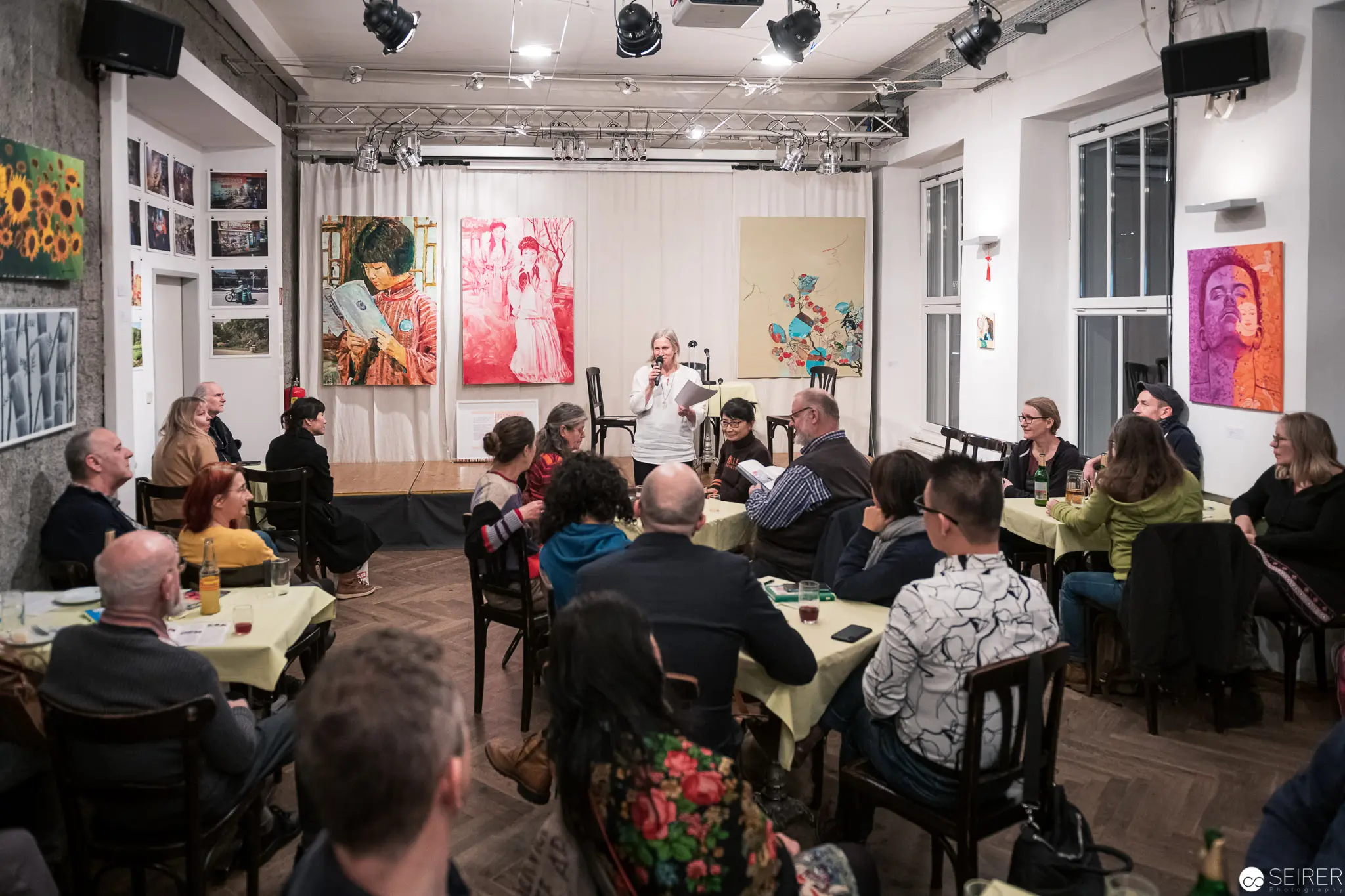 Art Gallery Talk: Audience Gathered in Intimate Exhibition Space with Colorful Portraits