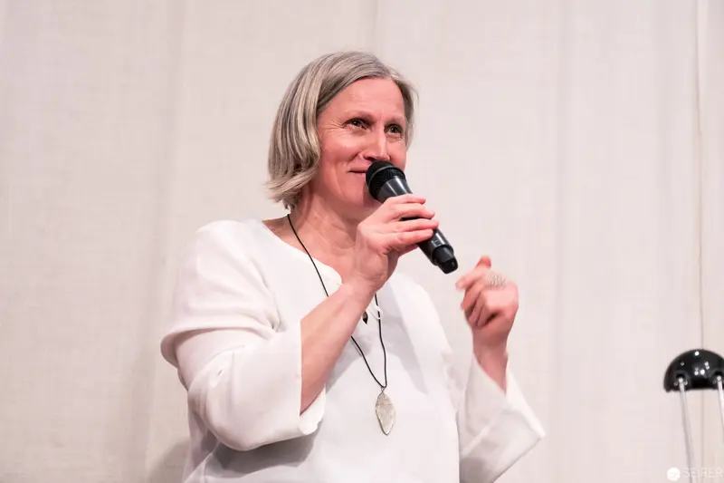 Woman in White Speaking at Podium with Wireless Microphone